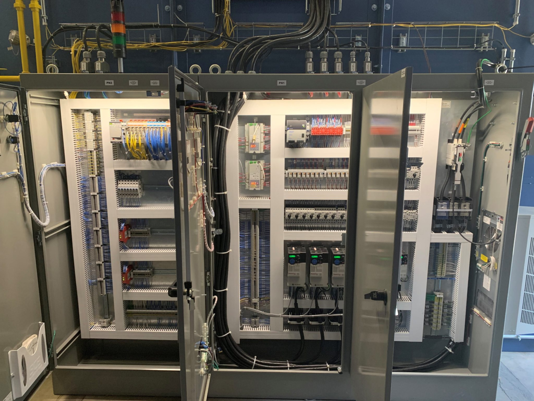 Internal view of the control panel for the DTI-1478 Annealing Batch Oven, showing a detailed arrangement of electrical components, wiring, and circuit boards. The panel's doors are open, revealing a complex system of wires, relays, and connectors, all meticulously organized. The various colored wires, labeled components, and mounted modules indicate the advanced control systems necessary for the operation of the industrial oven. Overhead, additional wiring and conduits are visible, contributing to the overall infrastructure of the equipment.